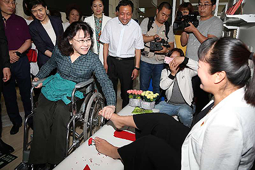 圖為張海迪與用腳剪剪紙、做絹花的殘疾人親切交談